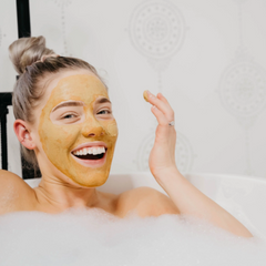 Woman with CLN & DRTY Glow Mask  in a bubble bath, smiling.