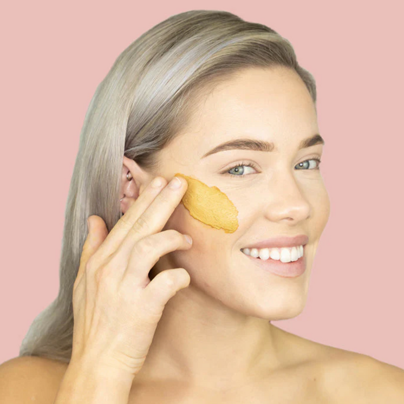 Woman applying CLN & DRTY Glow Mask to her left eye against a pink background