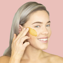 Woman applying CLN & DRTY Glow Mask to her left eye against a pink background