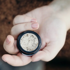 Hand holding a small container of beige powder against a blurred background