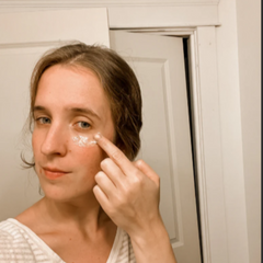 Person applying cream to their face in front of a mirror.