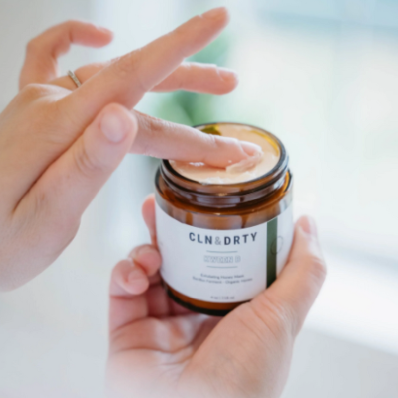 Person applying cream from a jar labeled 'CLN & DIRTY' with a blurred background