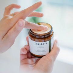 Person applying cream from a jar labeled 'CLN & DIRTY' with a blurred background