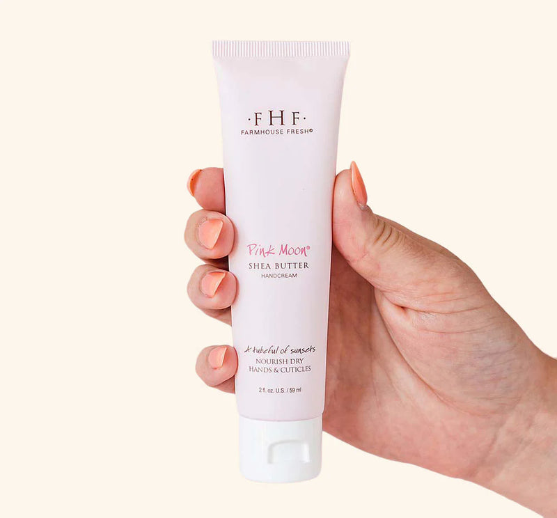 Hand holding a tube of Farmhouse Fresh Pink Moon Shea Butter Hand Cream against a white background