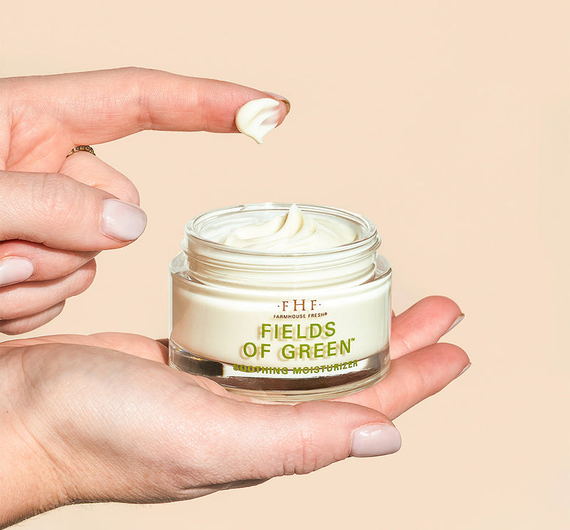 Hand holding a jar of 'Fields of Green' moisturizer with a beige background