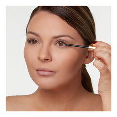 Woman applying mascara with a brush on a plain background