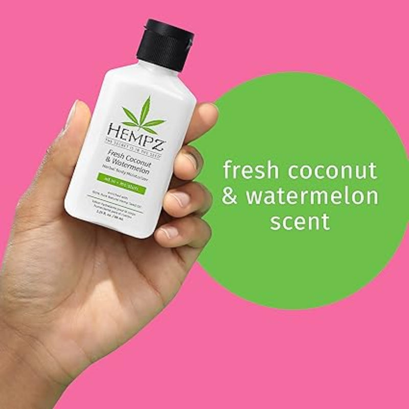 Hand holding a Hempz body wash bottle with a pink background and green text.
